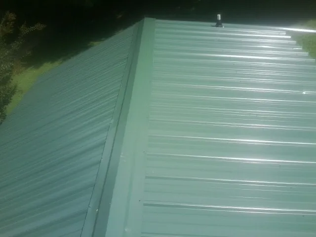 New green metal panels meeting at the ridge of a roof — Flat Roof Repair work by our crew in Fort Lauderdale