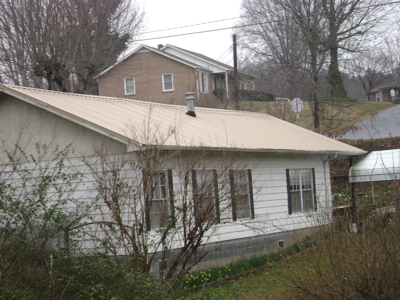Tan metal roof on a white sided house set into a hillside — Commercial Roofing by Roofing Brothers in Fort Lauderdale