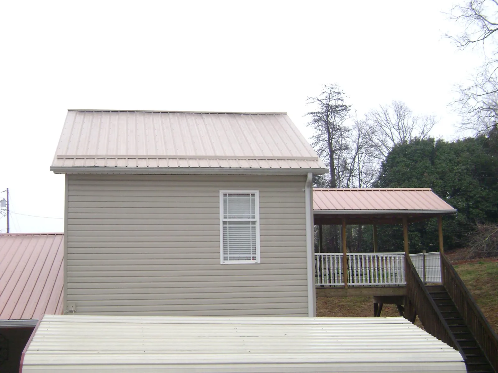 Tan metal roofs on a two story addition and attached porch, from a Roof Replacement job in Fort Lauderdale